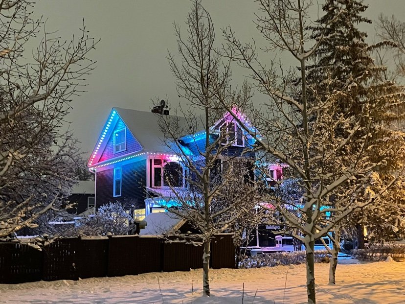 Design inspiration: home with multicolor roofline holiday lighting at night in the snow